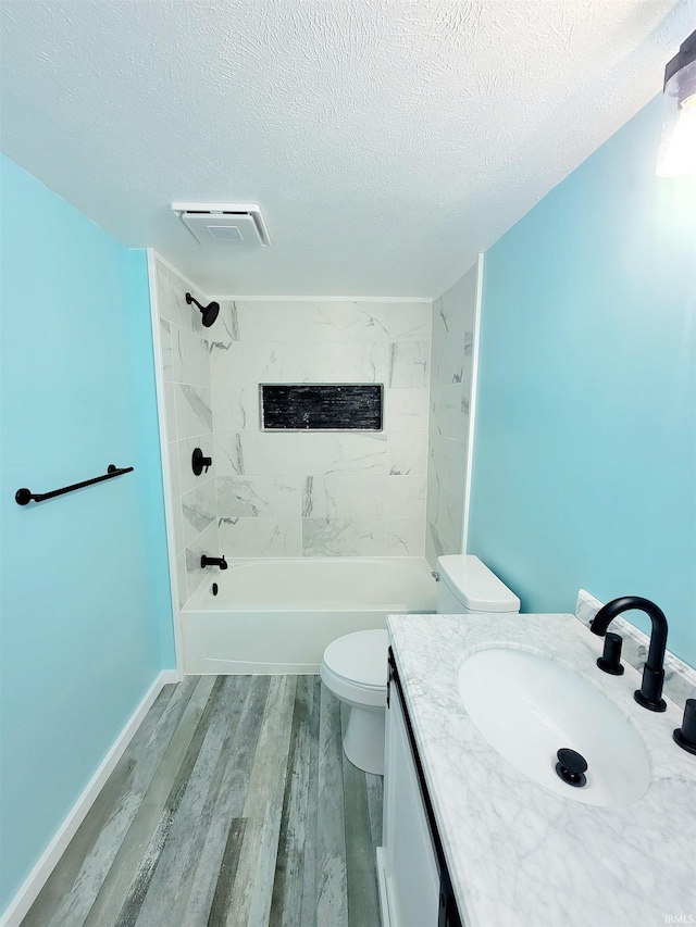 full bathroom with tiled shower / bath, vanity, wood-type flooring, a textured ceiling, and toilet