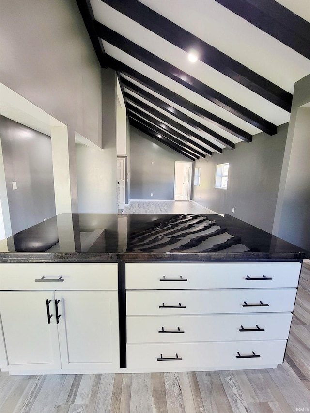 kitchen featuring light wood-type flooring, dark stone countertops, vaulted ceiling with beams, and white cabinetry