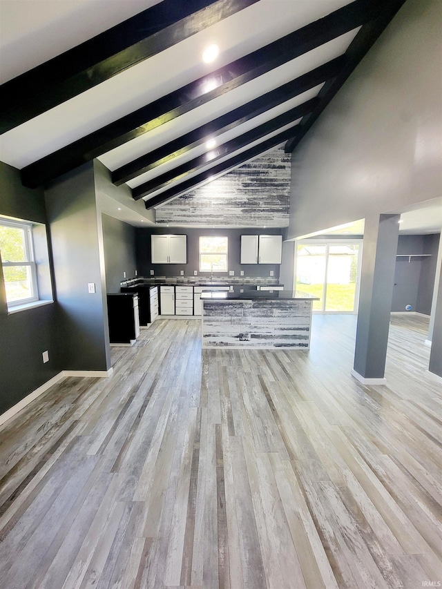 unfurnished living room featuring beamed ceiling, a healthy amount of sunlight, and light hardwood / wood-style floors