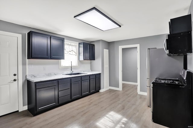 kitchen featuring light stone counters, black gas stove, light wood-type flooring, and sink