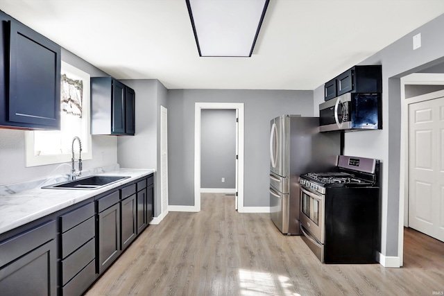 kitchen with appliances with stainless steel finishes, light stone counters, sink, and light hardwood / wood-style floors