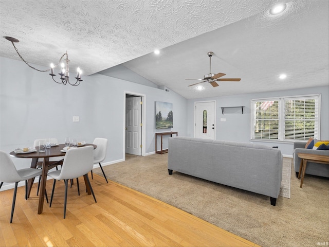 living room featuring hardwood / wood-style flooring, ceiling fan with notable chandelier, vaulted ceiling, and a textured ceiling