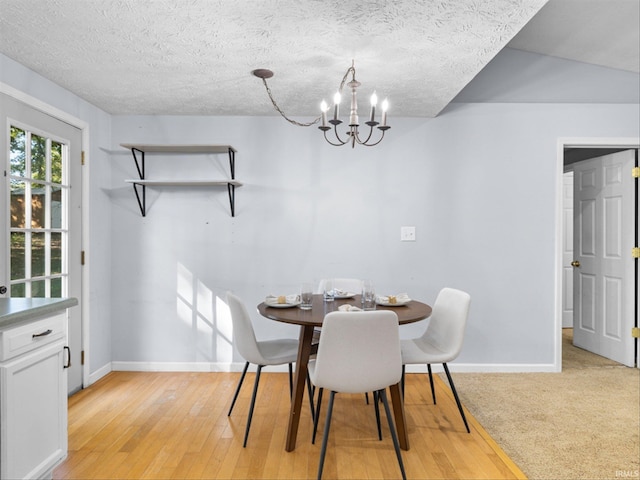 dining area with vaulted ceiling, a textured ceiling, a chandelier, and light hardwood / wood-style floors