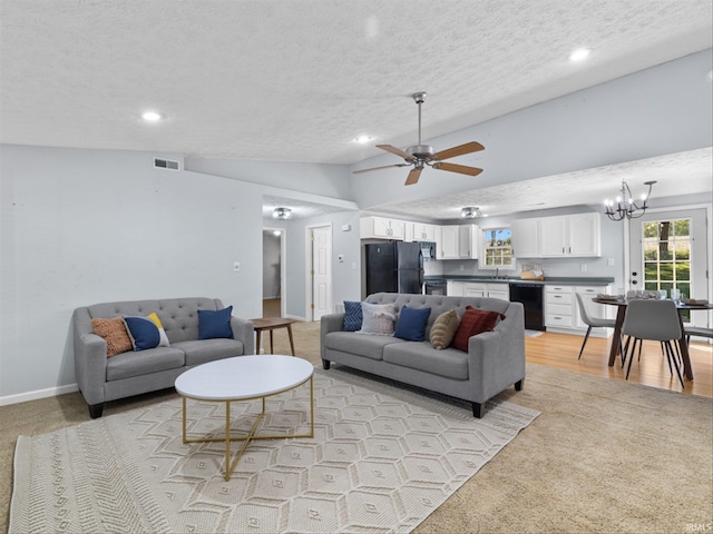 living room with ceiling fan with notable chandelier, lofted ceiling, light colored carpet, and a textured ceiling