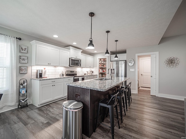 kitchen featuring a kitchen island with sink, dark wood-type flooring, light stone counters, appliances with stainless steel finishes, and white cabinetry