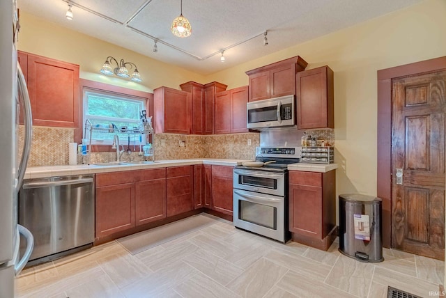 kitchen featuring sink, decorative light fixtures, rail lighting, appliances with stainless steel finishes, and decorative backsplash