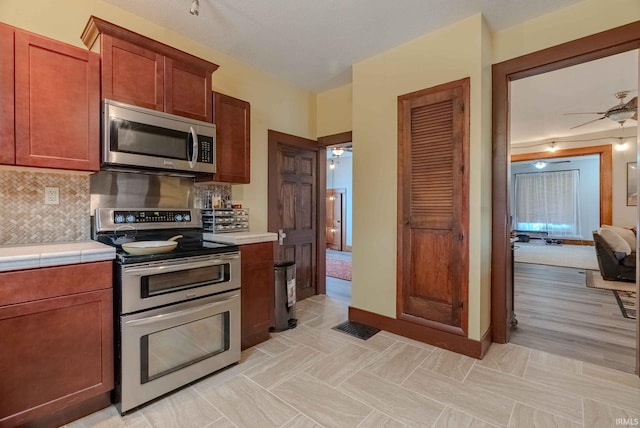 kitchen featuring ceiling fan, tasteful backsplash, appliances with stainless steel finishes, tile countertops, and light hardwood / wood-style floors