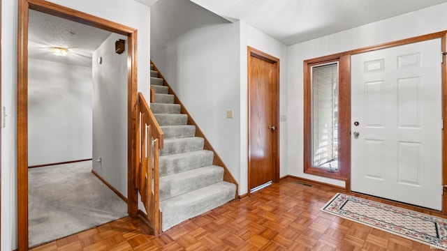 entrance foyer featuring stairs, visible vents, a textured ceiling, and baseboards