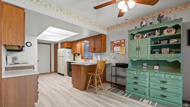 kitchen with light wood-style floors, ceiling fan, freestanding refrigerator, brown cabinetry, and a peninsula