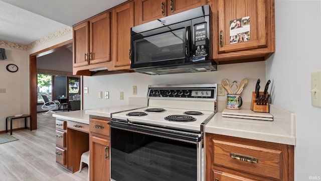 kitchen with electric range oven, light countertops, brown cabinets, black microwave, and light wood finished floors