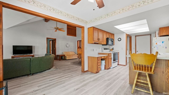 kitchen with ceiling fan, a skylight, white appliances, light hardwood / wood-style flooring, and high vaulted ceiling