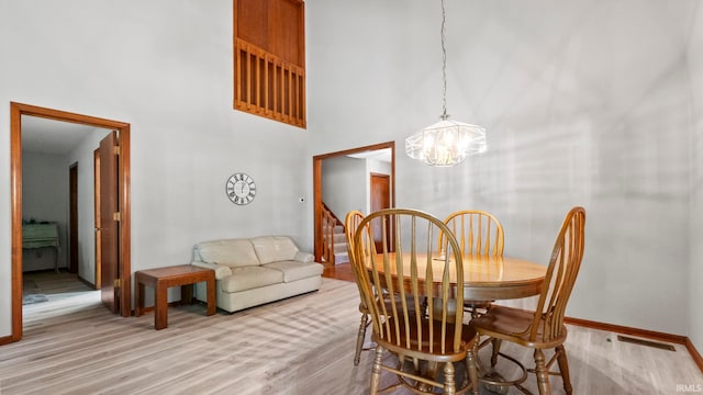 dining space with a towering ceiling, a notable chandelier, light wood-type flooring, and baseboards