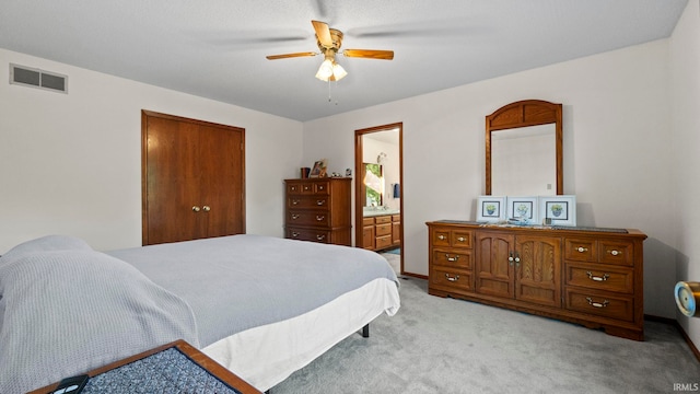 carpeted bedroom featuring a closet, ensuite bath, and ceiling fan