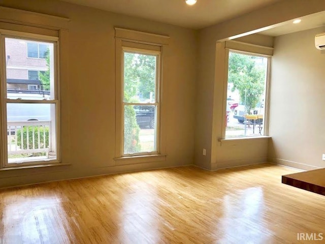 unfurnished room with a wall unit AC, light hardwood / wood-style flooring, and a healthy amount of sunlight