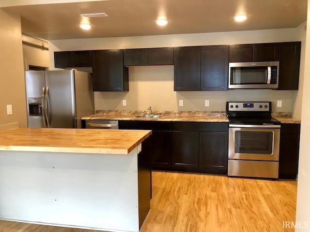 kitchen with wooden counters, light wood-type flooring, sink, appliances with stainless steel finishes, and a center island