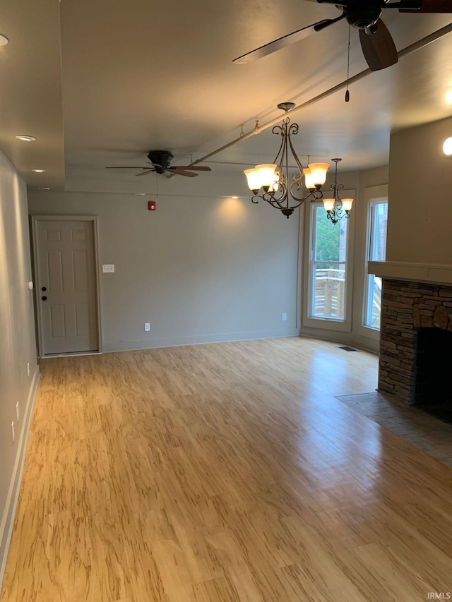 unfurnished living room with ceiling fan with notable chandelier, a fireplace, and light hardwood / wood-style floors