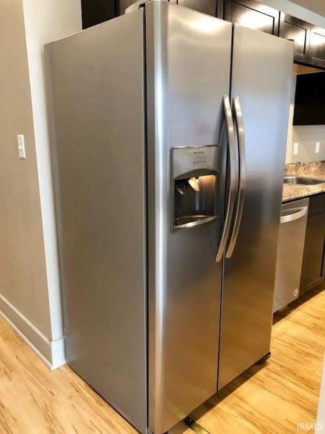 kitchen featuring appliances with stainless steel finishes, light stone countertops, sink, and light hardwood / wood-style flooring