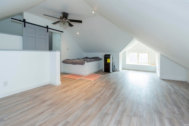 additional living space with ceiling fan, light hardwood / wood-style flooring, a barn door, and lofted ceiling