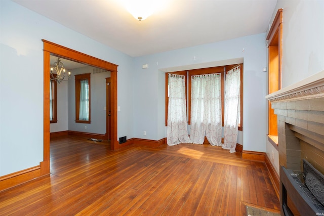 unfurnished living room with a notable chandelier, wood-type flooring, and a brick fireplace