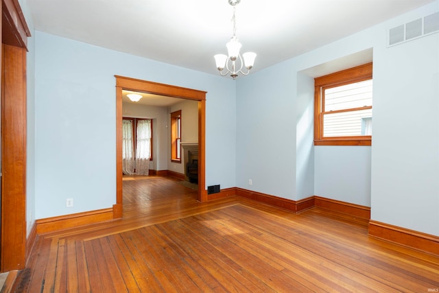 unfurnished room with a notable chandelier, plenty of natural light, and hardwood / wood-style floors