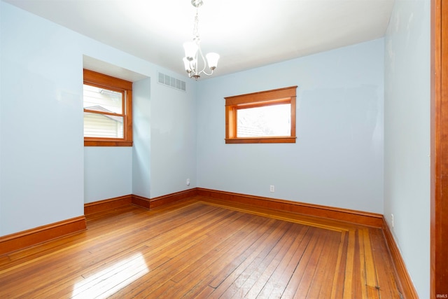 unfurnished room with hardwood / wood-style floors, an inviting chandelier, and a wealth of natural light