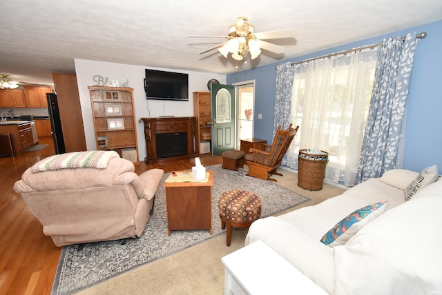 living room with ceiling fan, a textured ceiling, sink, and light hardwood / wood-style floors