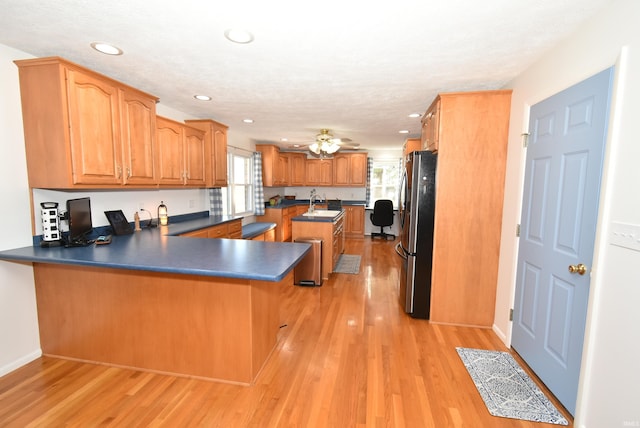 kitchen with ceiling fan, stainless steel refrigerator, sink, light hardwood / wood-style floors, and kitchen peninsula