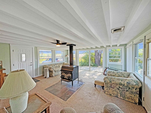 sunroom / solarium featuring a wood stove, beamed ceiling, plenty of natural light, and ceiling fan