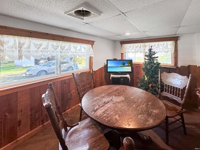 carpeted dining area with a paneled ceiling and wood walls