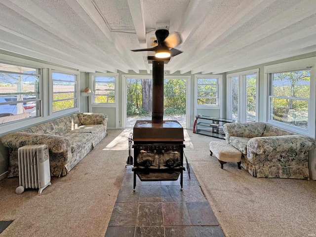 sunroom / solarium with a wood stove, beam ceiling, a healthy amount of sunlight, and radiator