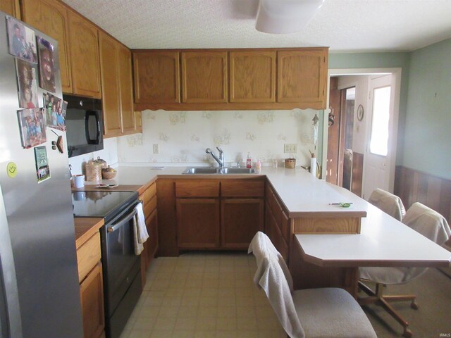 kitchen with black appliances, a breakfast bar, sink, kitchen peninsula, and a textured ceiling