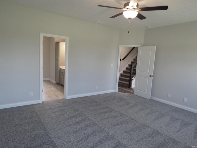 unfurnished room featuring ceiling fan, stairway, light colored carpet, and baseboards