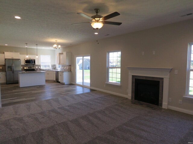 unfurnished living room featuring dark carpet, a wealth of natural light, a fireplace with flush hearth, and baseboards