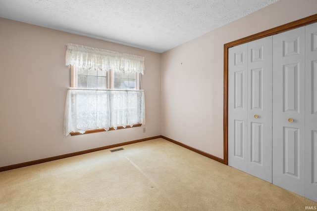 unfurnished bedroom featuring light colored carpet, a closet, and a textured ceiling