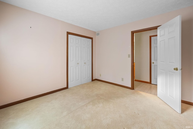 unfurnished bedroom featuring light colored carpet, a textured ceiling, and a closet