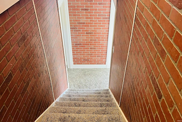 stairs featuring carpet floors and brick wall