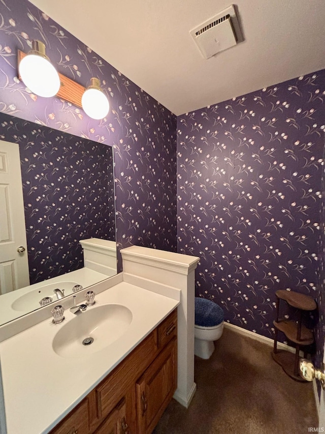 half bath with wallpapered walls, baseboards, visible vents, toilet, and vanity