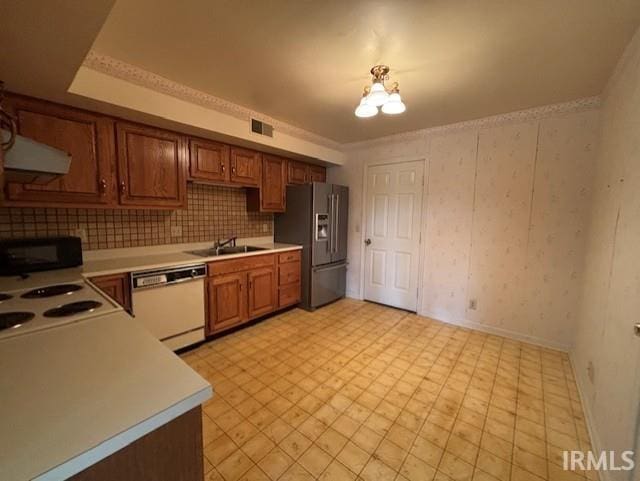 kitchen with range hood, light countertops, white dishwasher, a sink, and stainless steel fridge