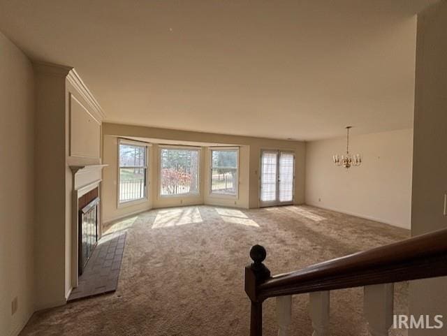 unfurnished living room featuring a tiled fireplace, carpet flooring, and a notable chandelier