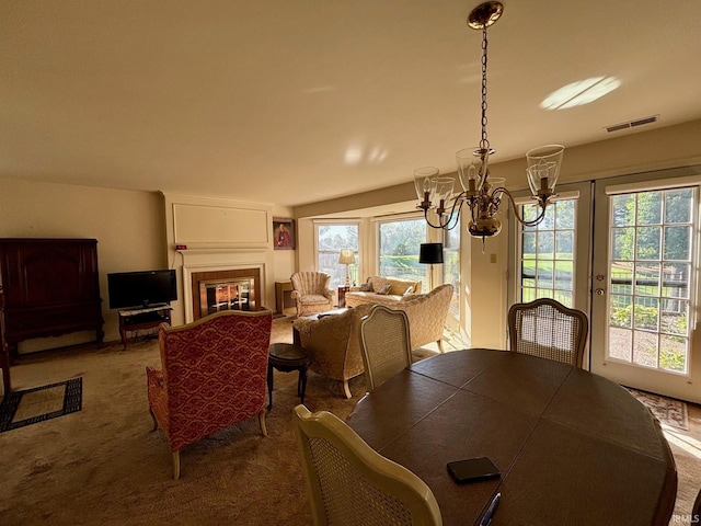 carpeted dining space featuring a fireplace, vaulted ceiling, a notable chandelier, and a wealth of natural light