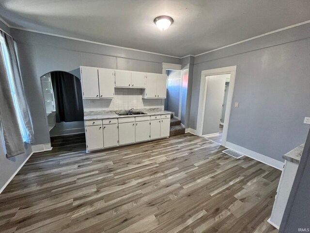 kitchen featuring sink, decorative backsplash, ornamental molding, hardwood / wood-style flooring, and white cabinetry