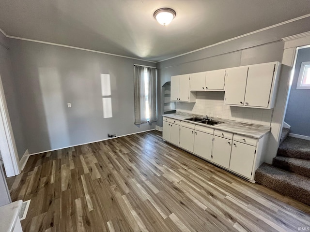 kitchen with light hardwood / wood-style floors, tasteful backsplash, crown molding, sink, and white cabinetry