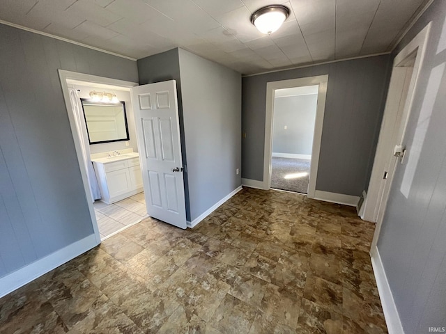 unfurnished bedroom with ornamental molding, wooden walls, ensuite bath, and sink