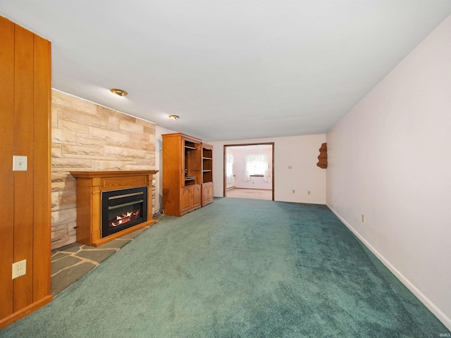 unfurnished living room featuring dark colored carpet, wood walls, and a stone fireplace