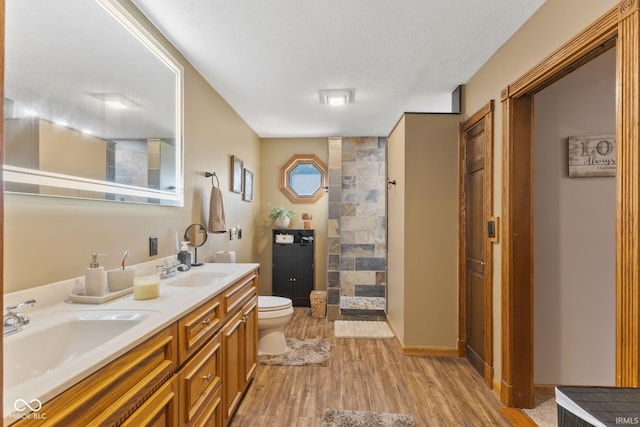 bathroom featuring walk in shower, toilet, hardwood / wood-style floors, vanity, and a textured ceiling