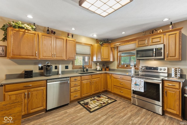 kitchen with light hardwood / wood-style floors, a textured ceiling, appliances with stainless steel finishes, and sink