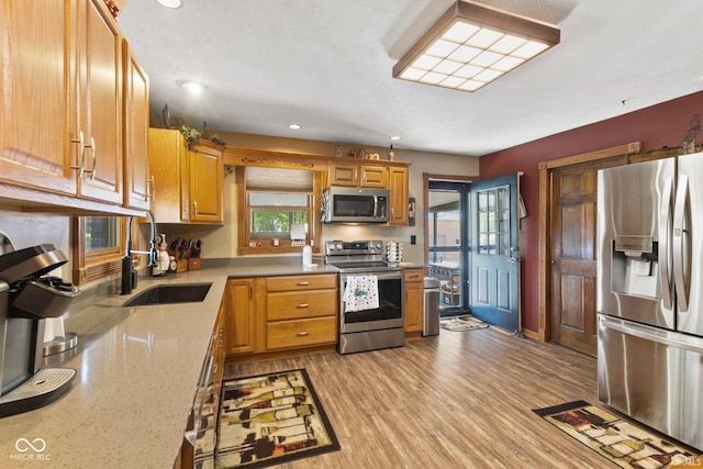 kitchen with light stone counters, sink, light hardwood / wood-style flooring, appliances with stainless steel finishes, and a textured ceiling