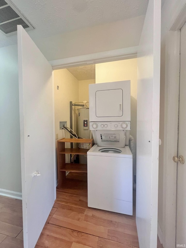 laundry area with electric water heater, light wood-type flooring, and stacked washing maching and dryer