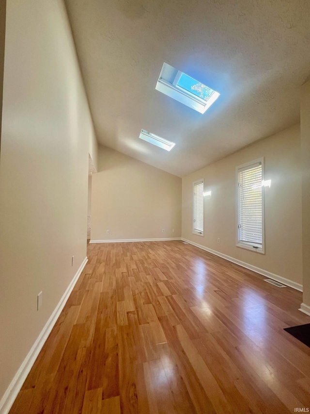 bonus room featuring light hardwood / wood-style floors, vaulted ceiling with skylight, and a textured ceiling