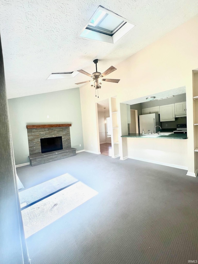 unfurnished living room featuring a skylight, a stone fireplace, a textured ceiling, carpet floors, and ceiling fan